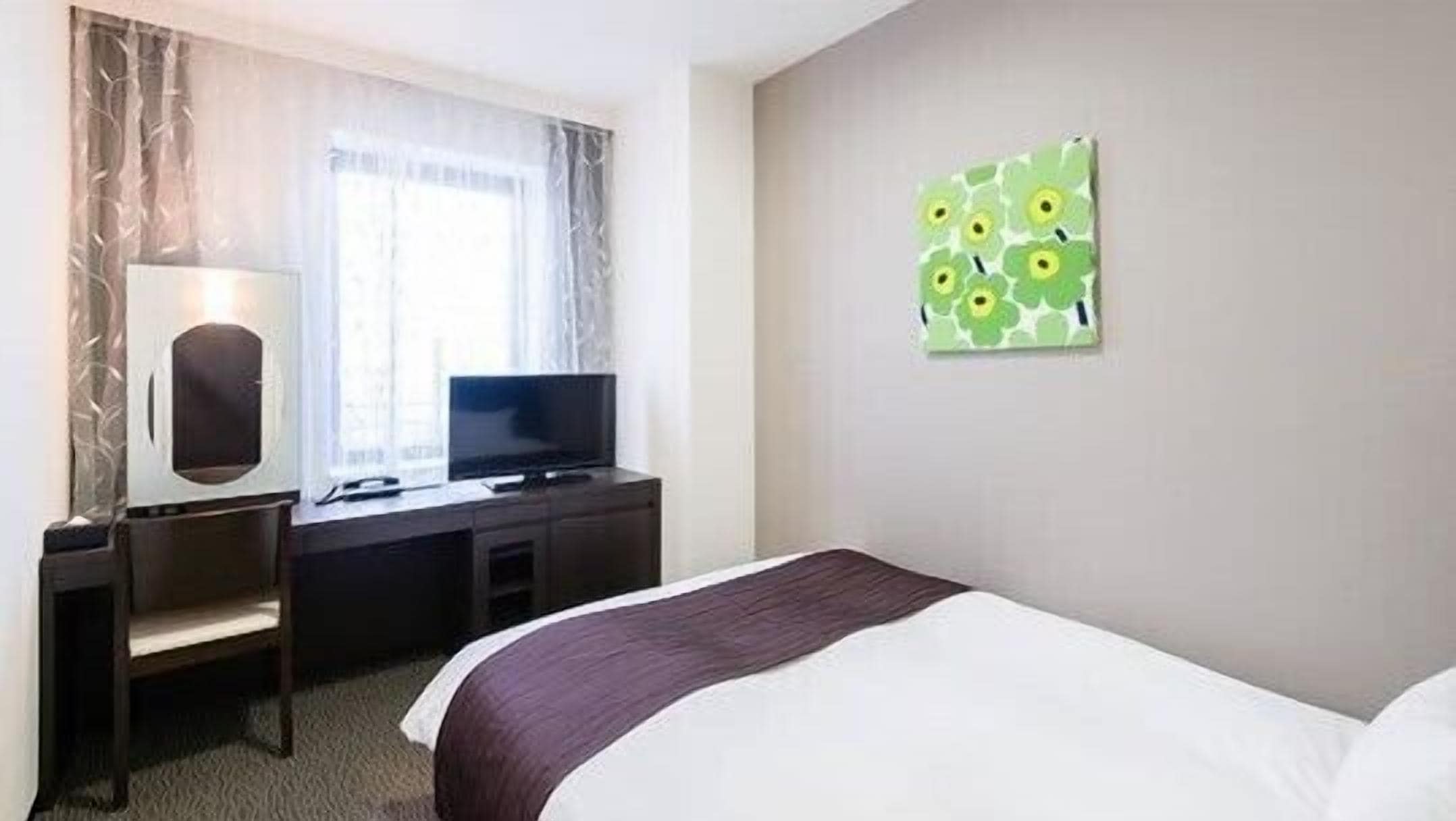 A hotel room with a bed, a desk with a television, and a wall-mounted artwork.
