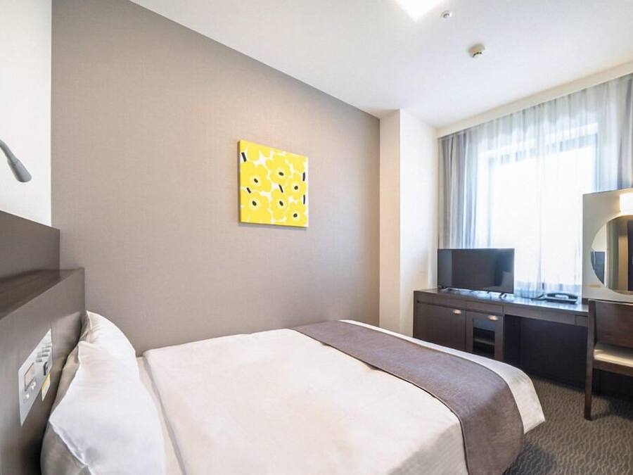 Habitación de hotel con cama, escritorio con televisor, espejo y ventana con cortinas.