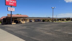 A Budget Inn with a red sign, a parking lot, and a building with a red roof. - Budget Inn (Tucumcari)