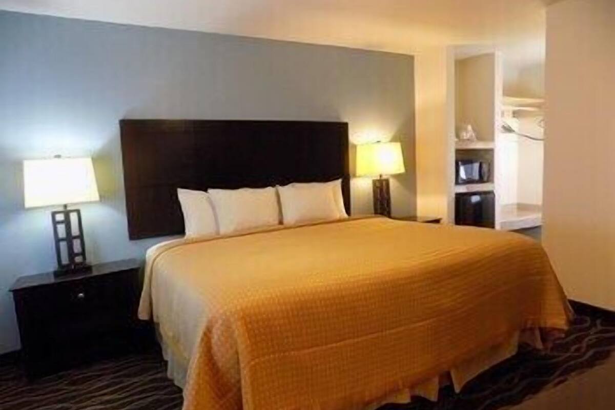 A hotel room with a bed, nightstands, a lamp, and a wall-mounted shelf.