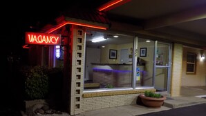 A building with a neon 'VACANCY' sign, a brick facade, and a large window. - Budget Inn (Tucumcari)