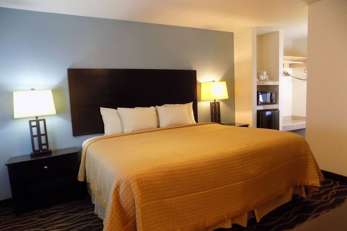 A hotel room with a bed, two bedside lamps, a nightstand, a dresser, and a microwave in the corner.
