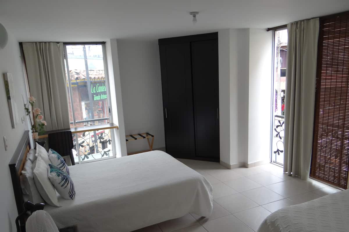 Un dormitorio con dos camas, una ventana con cortinas, un armario oscuro y un balcón con vista a la calle.