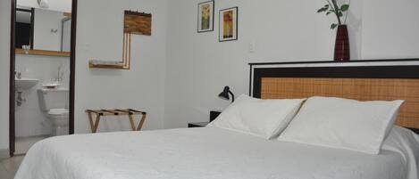 Une chambre à coucher avec un grand lit, une table de chevet, un miroir, une petite table et un vase rempli de fleurs.