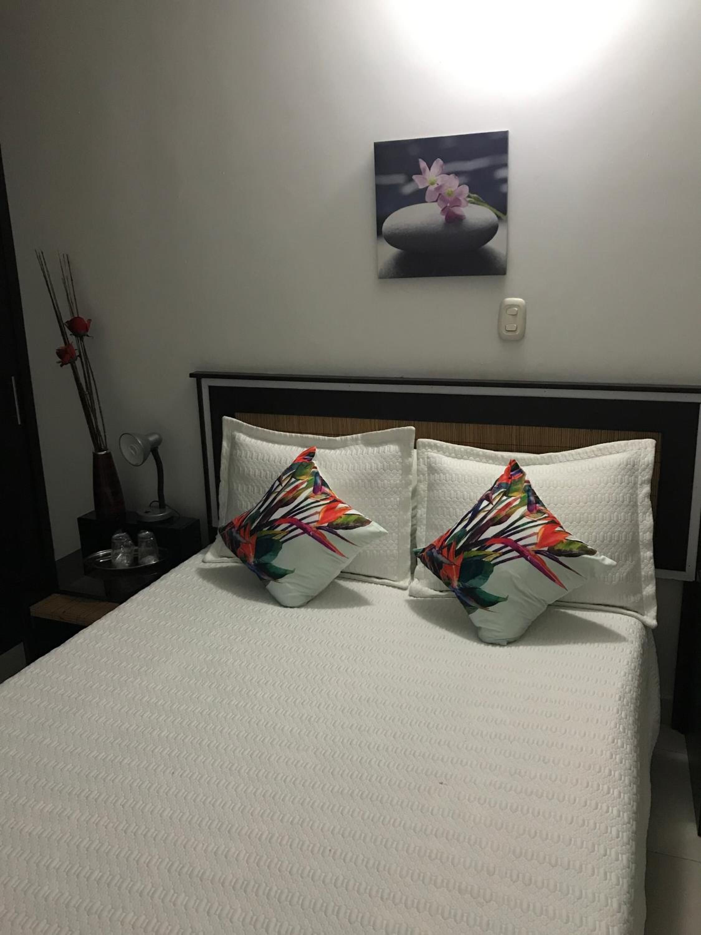 A neatly made bed with white bedding and two decorative pillows with a tropical leaf pattern.