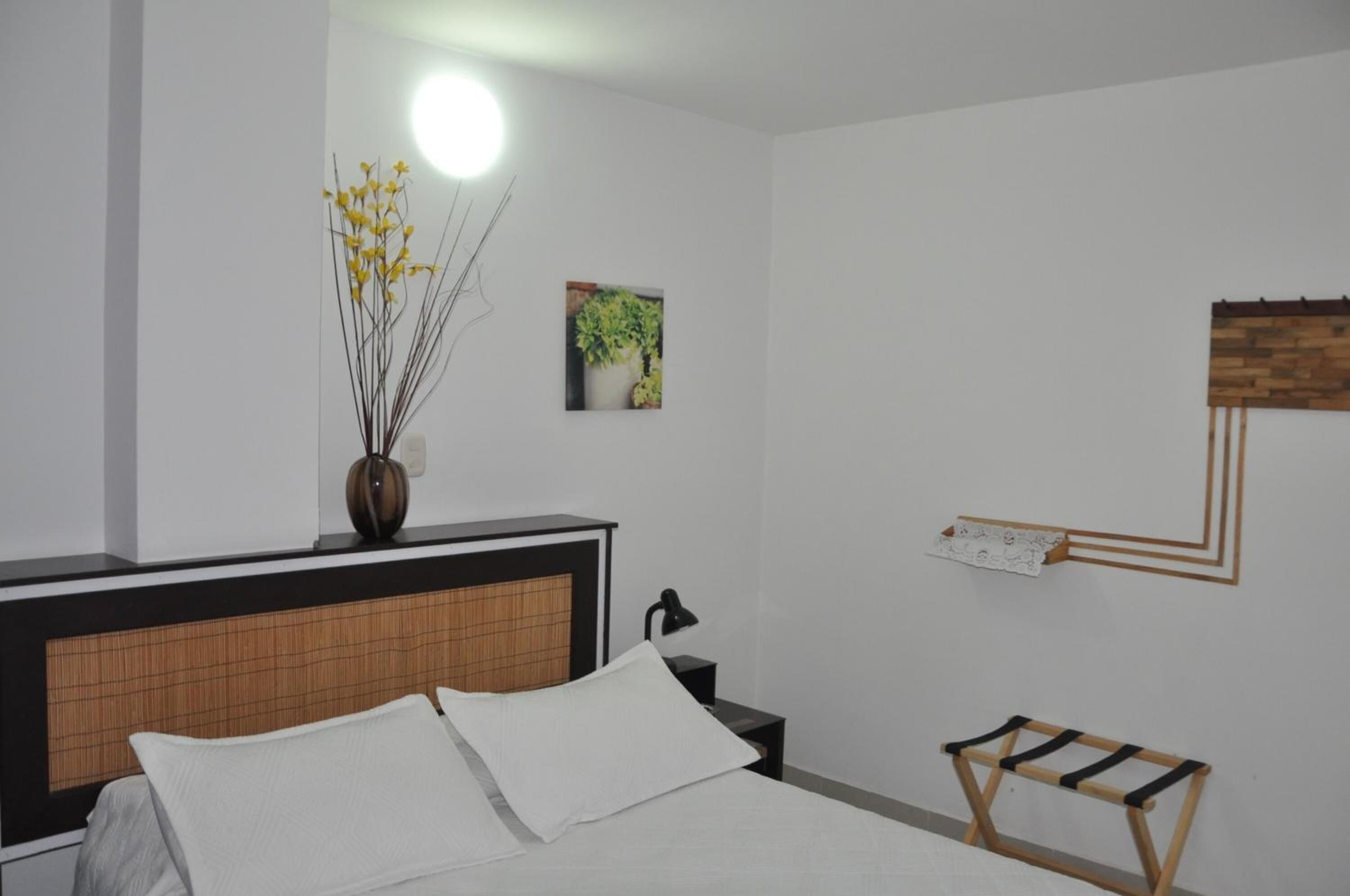 Een slaapkamer met een bed, nachtkastje, lamp, wandplank en een kunstwerk aan de muur.