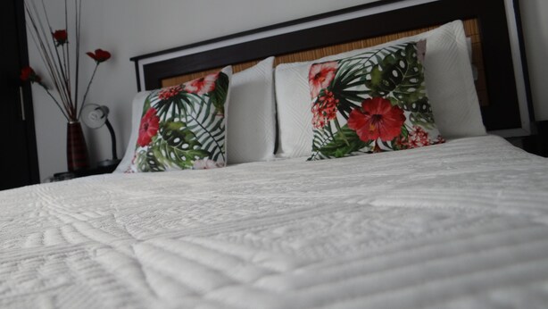 Un lit bien fait, avec une couette blanche et deux coussins à motifs floraux.