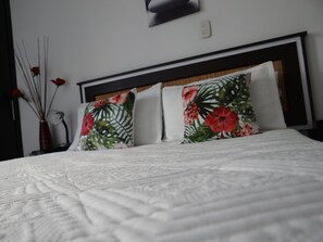 Un lit bien fait, avec une couette blanche et deux coussins à motifs floraux.