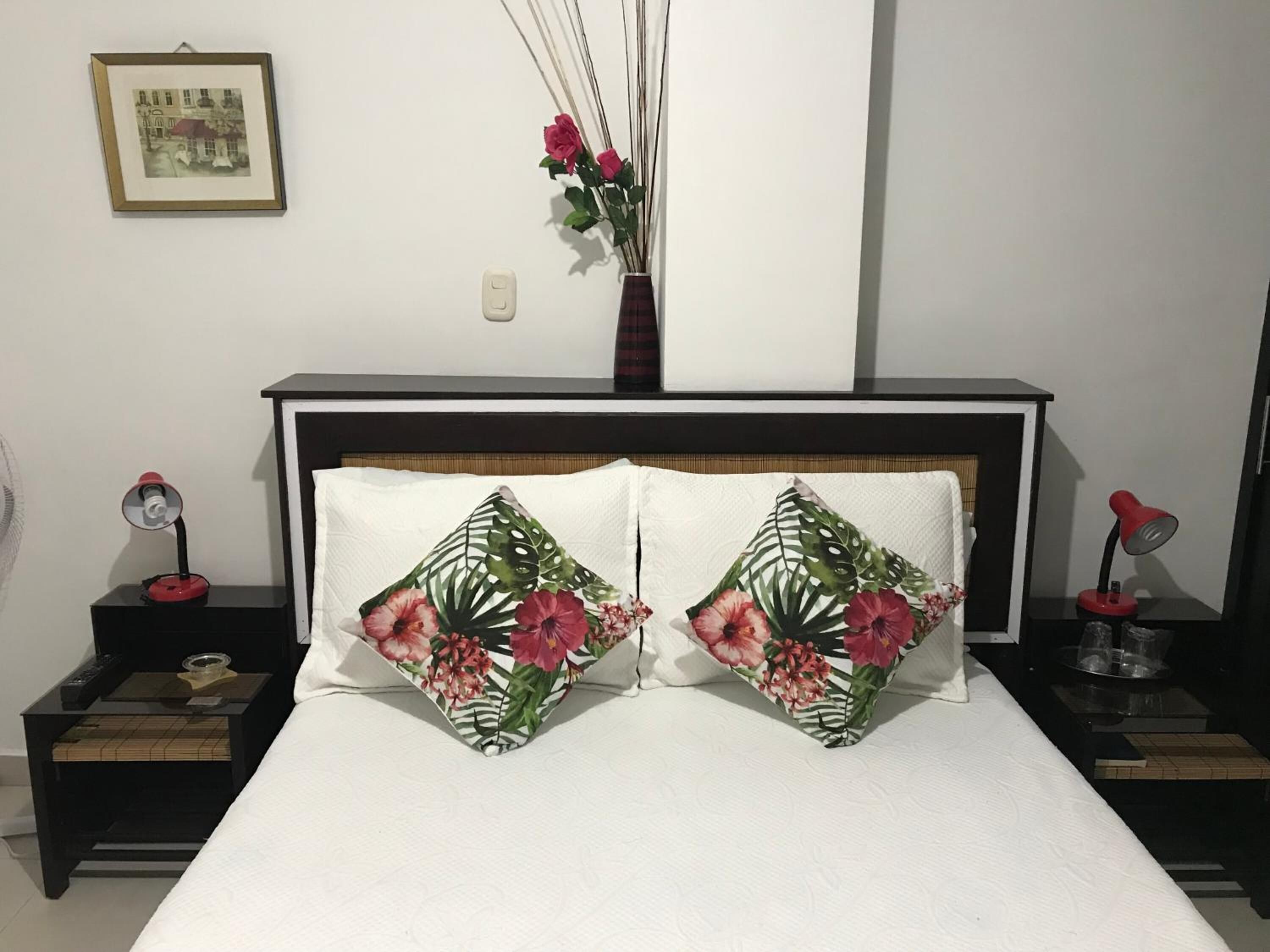 A neatly made bed with two decorative pillows, a bedside table with a lamp, and a wall-mounted picture.