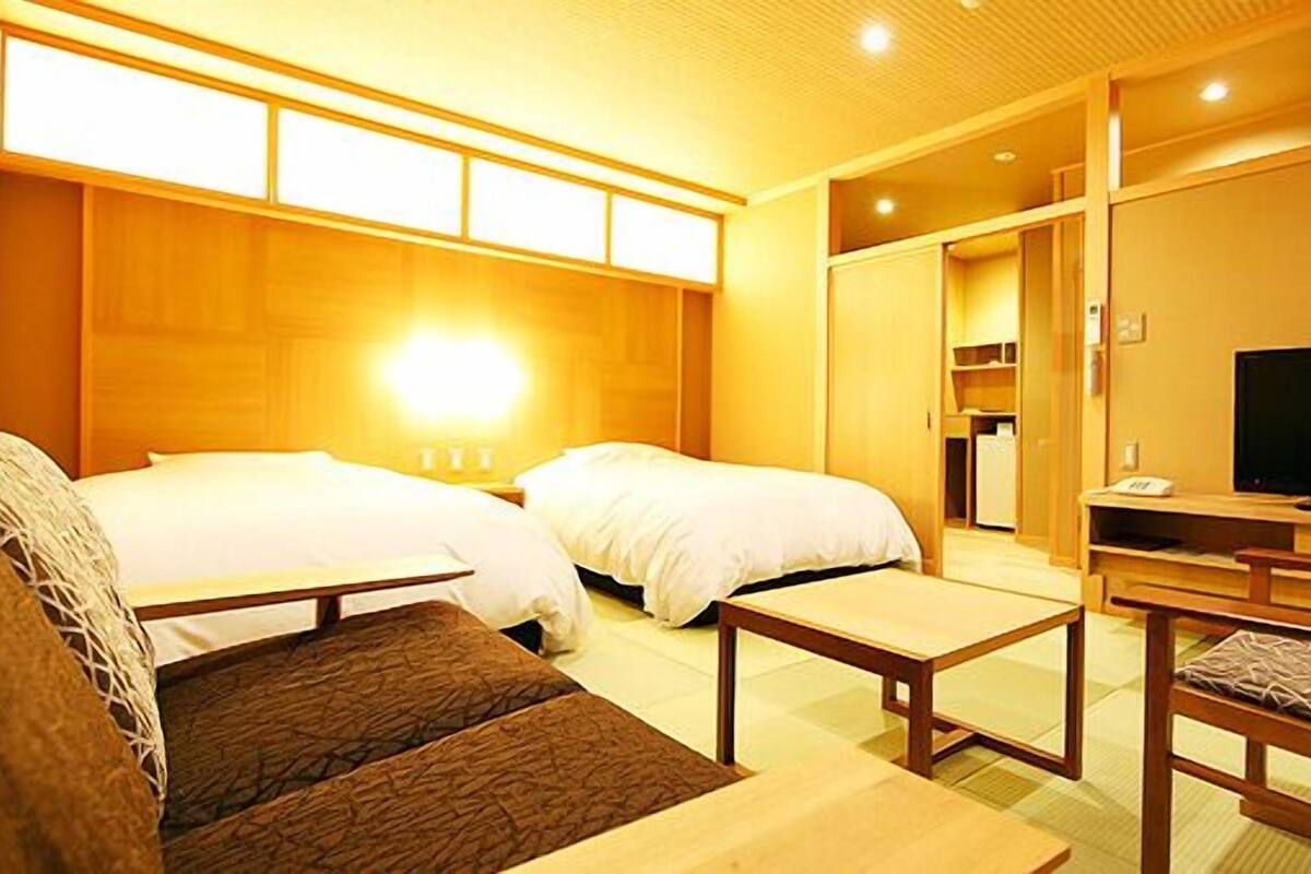 A hotel room with two beds, a TV, a sofa, and a wooden cabinet.