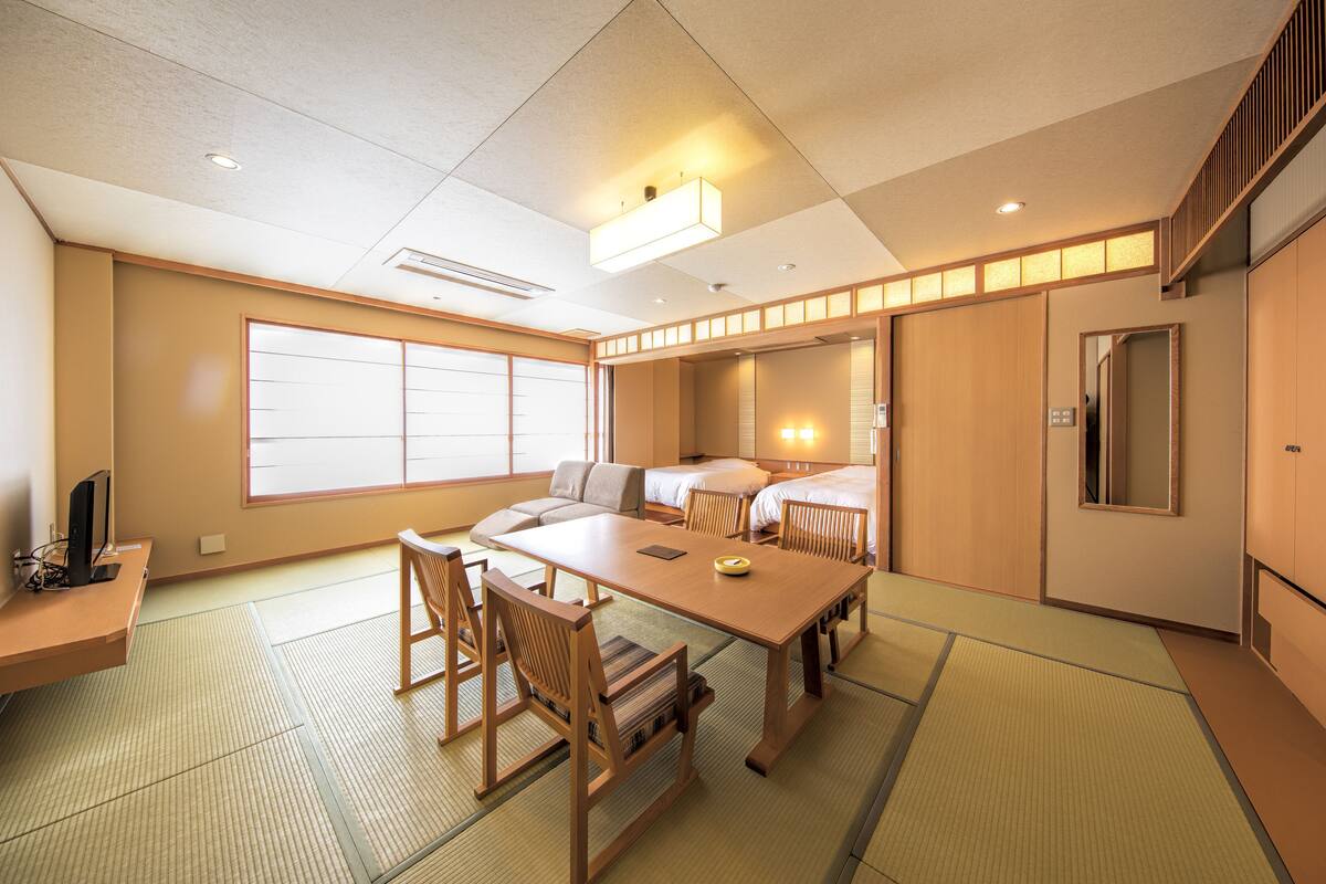 A traditional Japanese-style room with tatami flooring, a low table, chairs, a bed, and sliding doors.