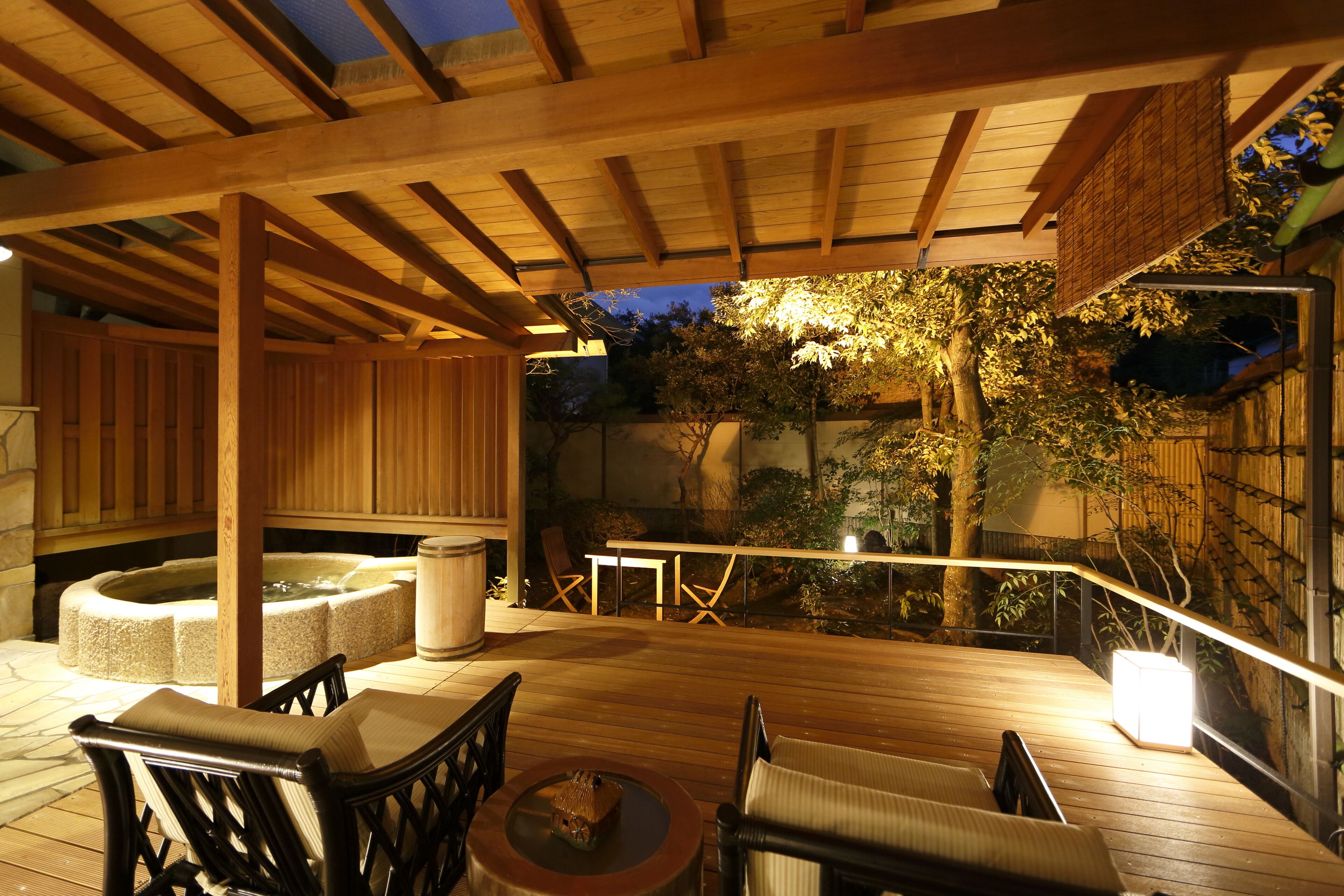 Une terrasse en bois avec des sièges d’extérieur, un jacuzzi et un bac à fleurs en pierre.