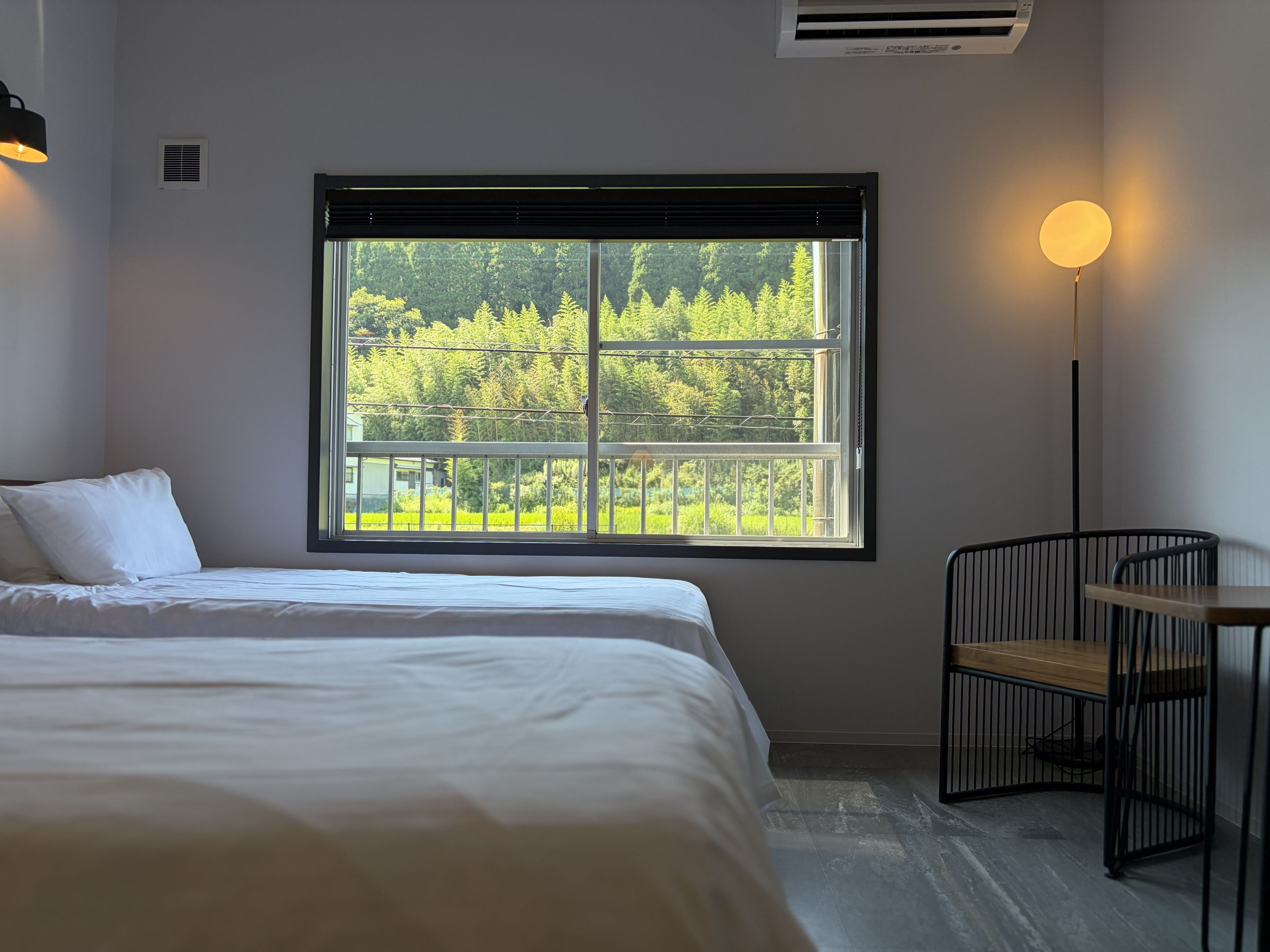 Ein Schlafzimmer mit großem Fenster, einem Bett, einem Sessel und einem Nachttisch.