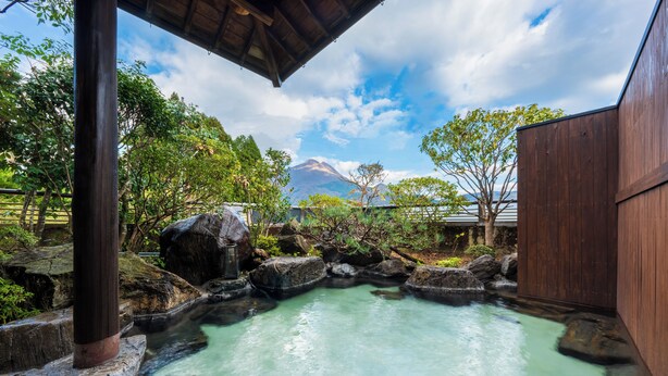 A traditional Japanese onsen with a wooden structure, a natural rock pool, and a mountain in the background. - Ryokan Hachisunoito (Yufu)