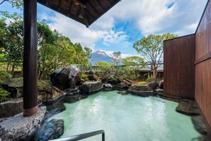 A traditional Japanese onsen with a wooden structure, a natural rock pool, and a mountain in the background.