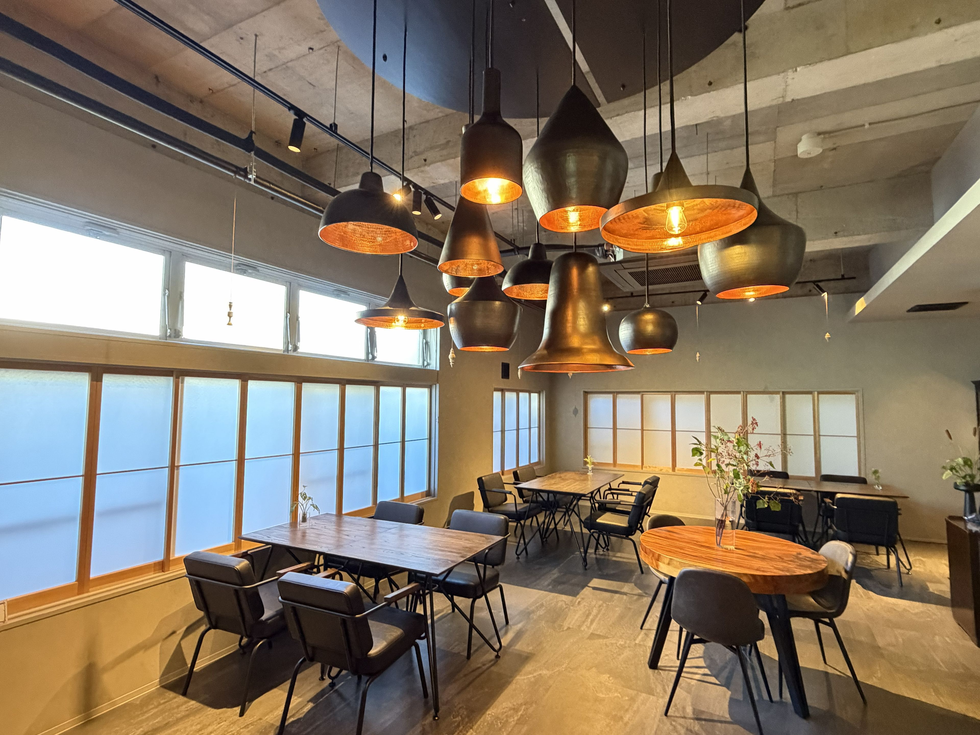 A modern conference room with large windows, multiple tables, and hanging pendant lights.