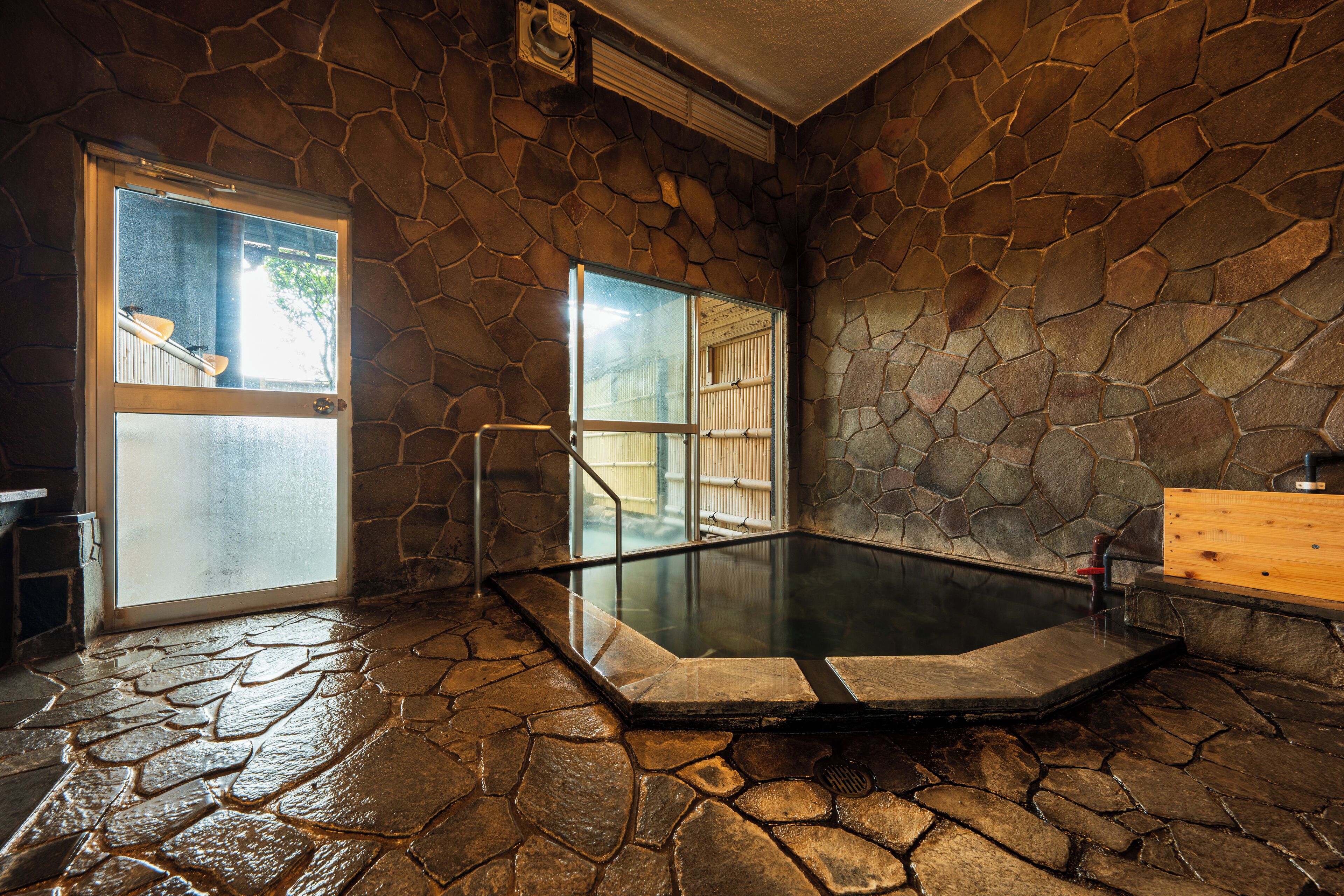 A stone-walled hot tub area with a glass door leading outside.