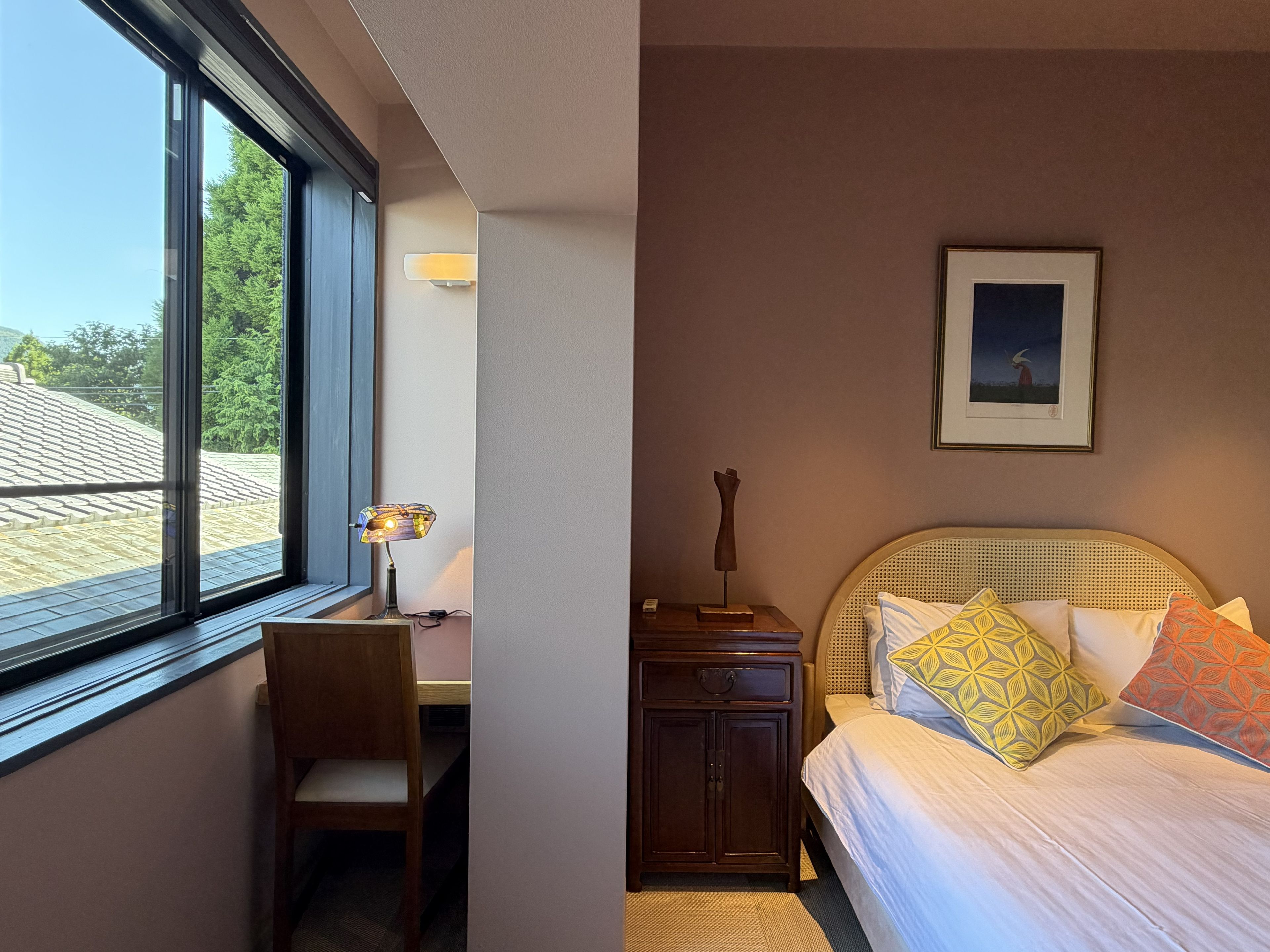 Ein Hotelzimmer mit Bett, Schreibtisch, Stuhl, Nachttisch, Lampe und einem gerahmten Bild an der Wand.