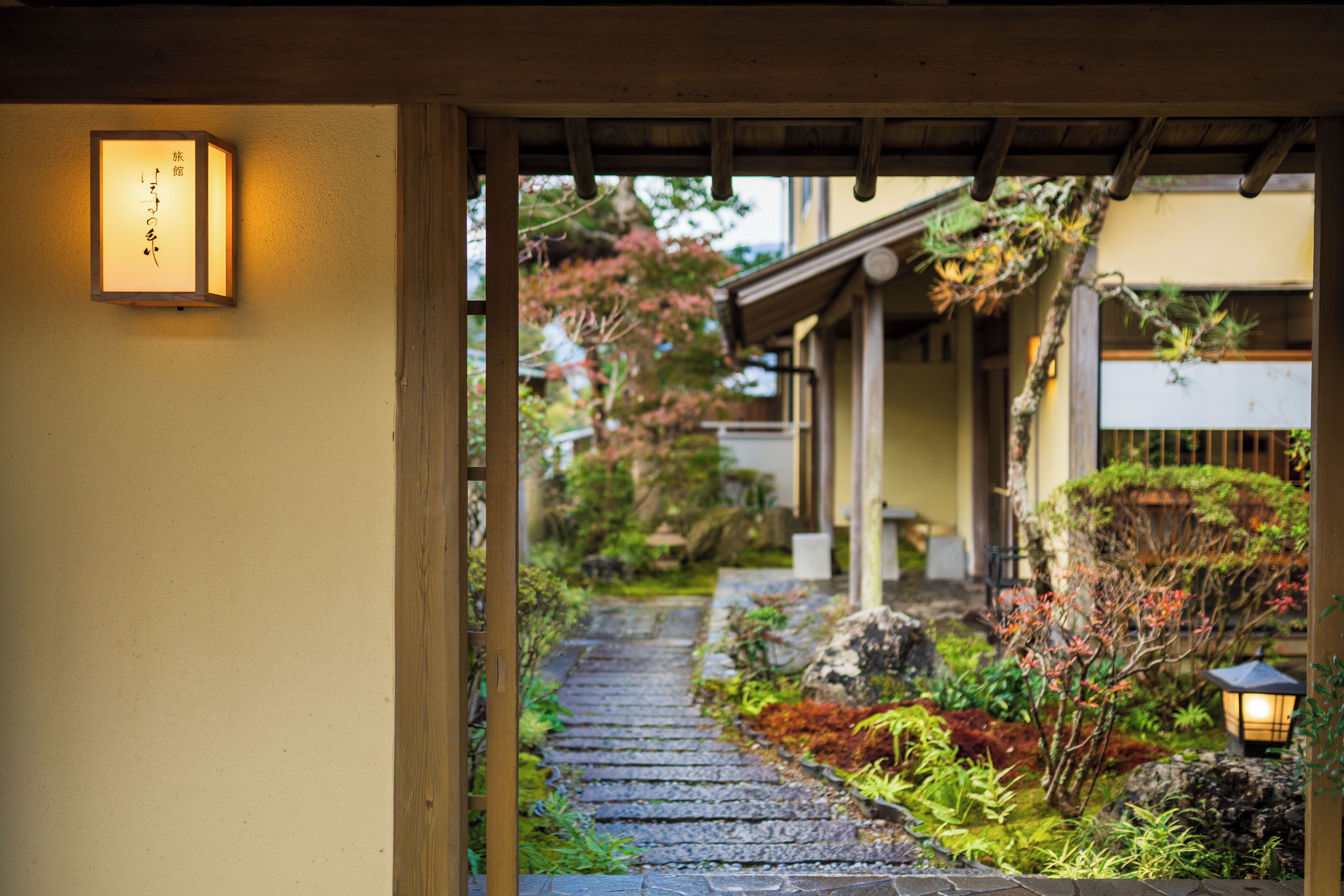 A traditional Japanese garden pathway leading to a building with a wooden structure and a lantern.