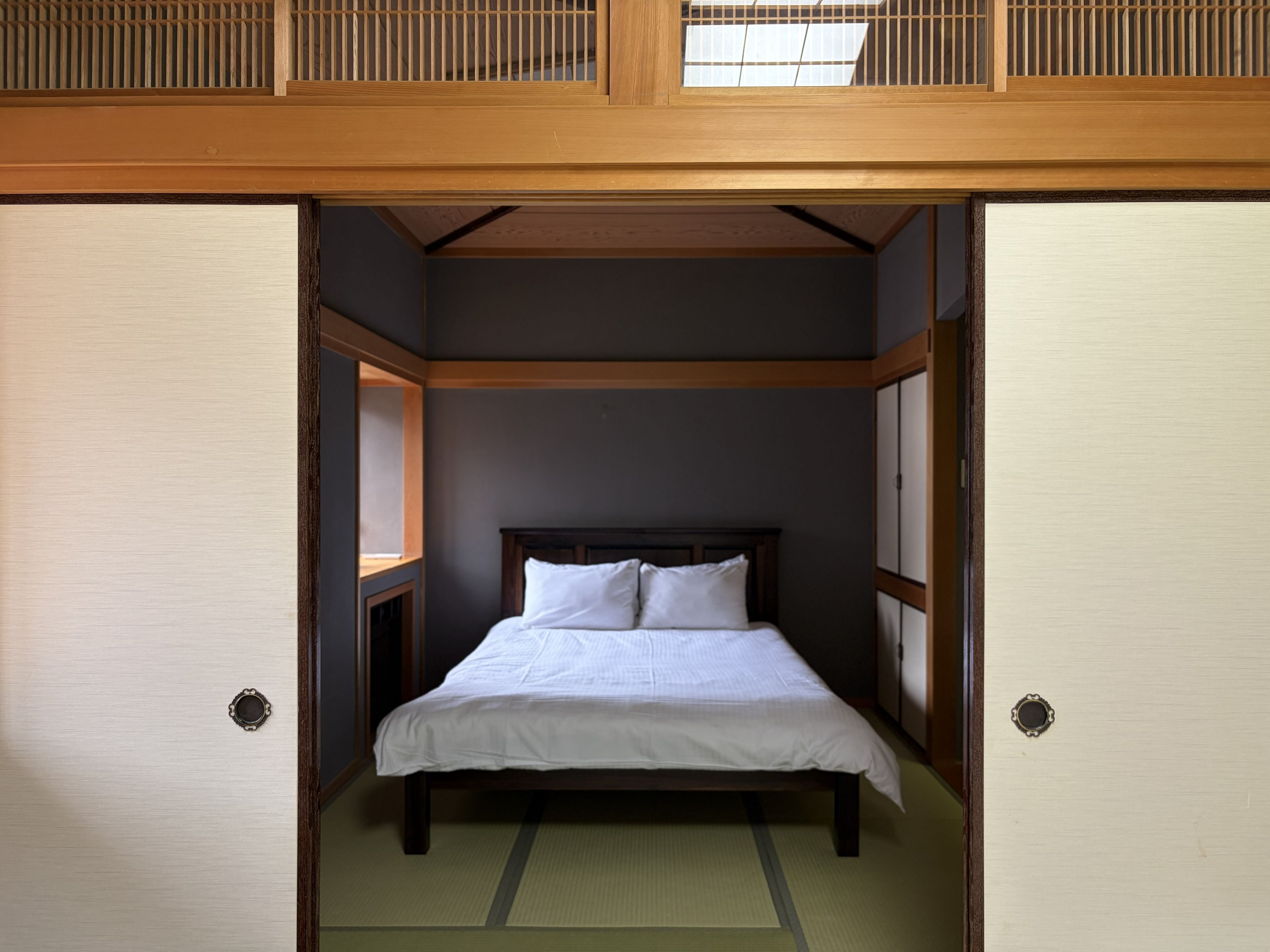 A traditional Japanese-style room with tatami flooring, a low wooden bed, and sliding doors.