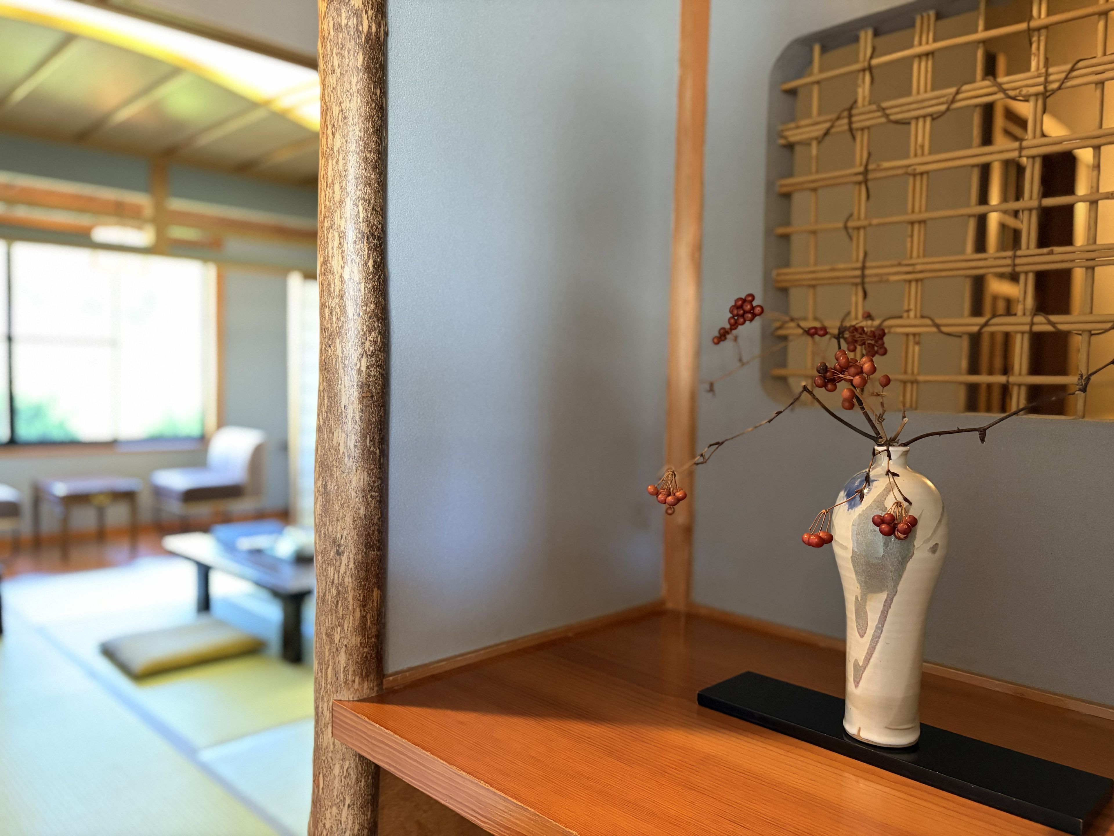 A traditional Japanese interior with a wooden table, a white vase with red berries, and a bamboo lattice wall.