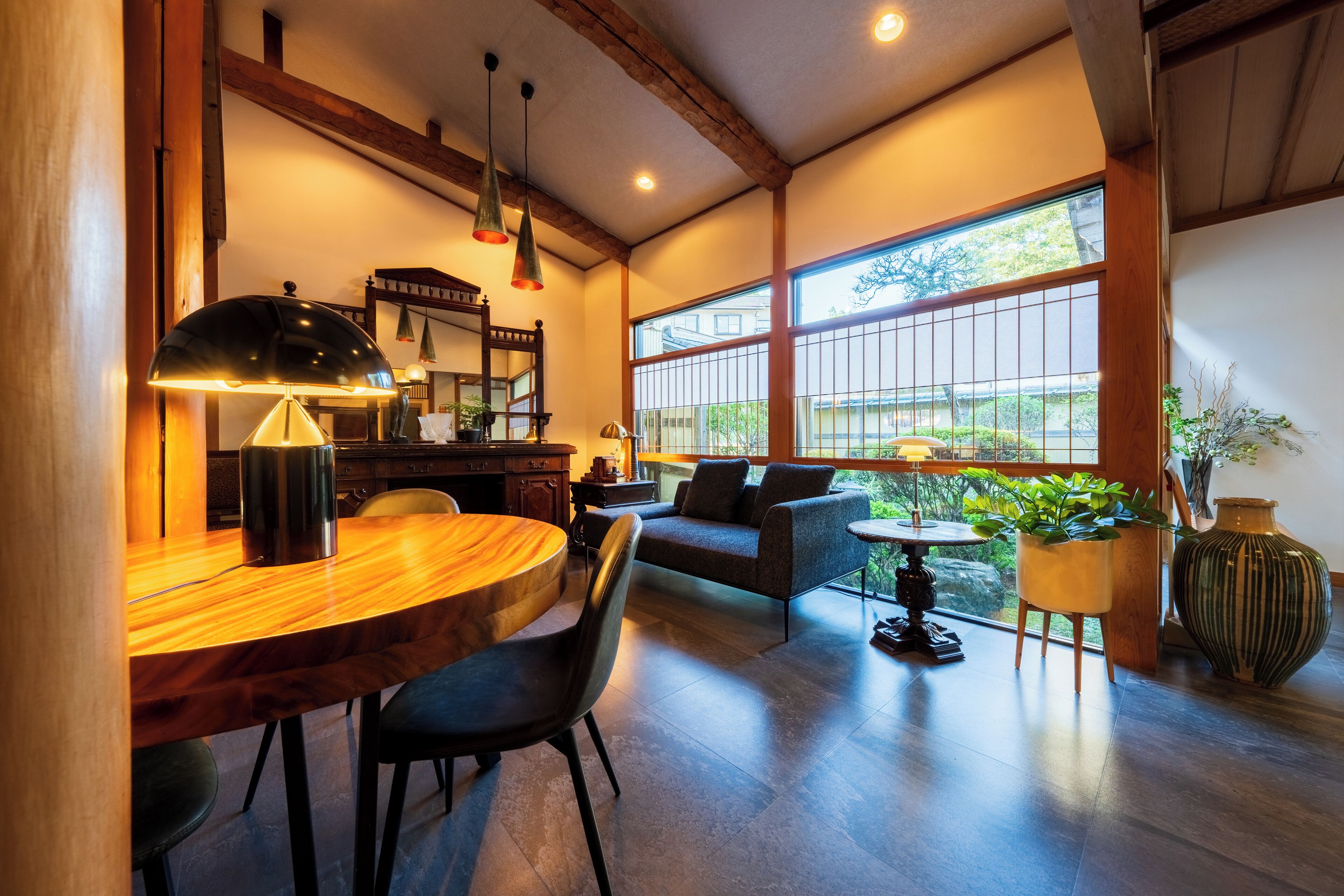 A spacious room with a wooden dining table, black chairs, a sofa, and a large window offering a view of the outdoors.