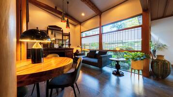 A spacious room with a wooden dining table, black chairs, a sofa, and a large window offering a view of the outdoors.