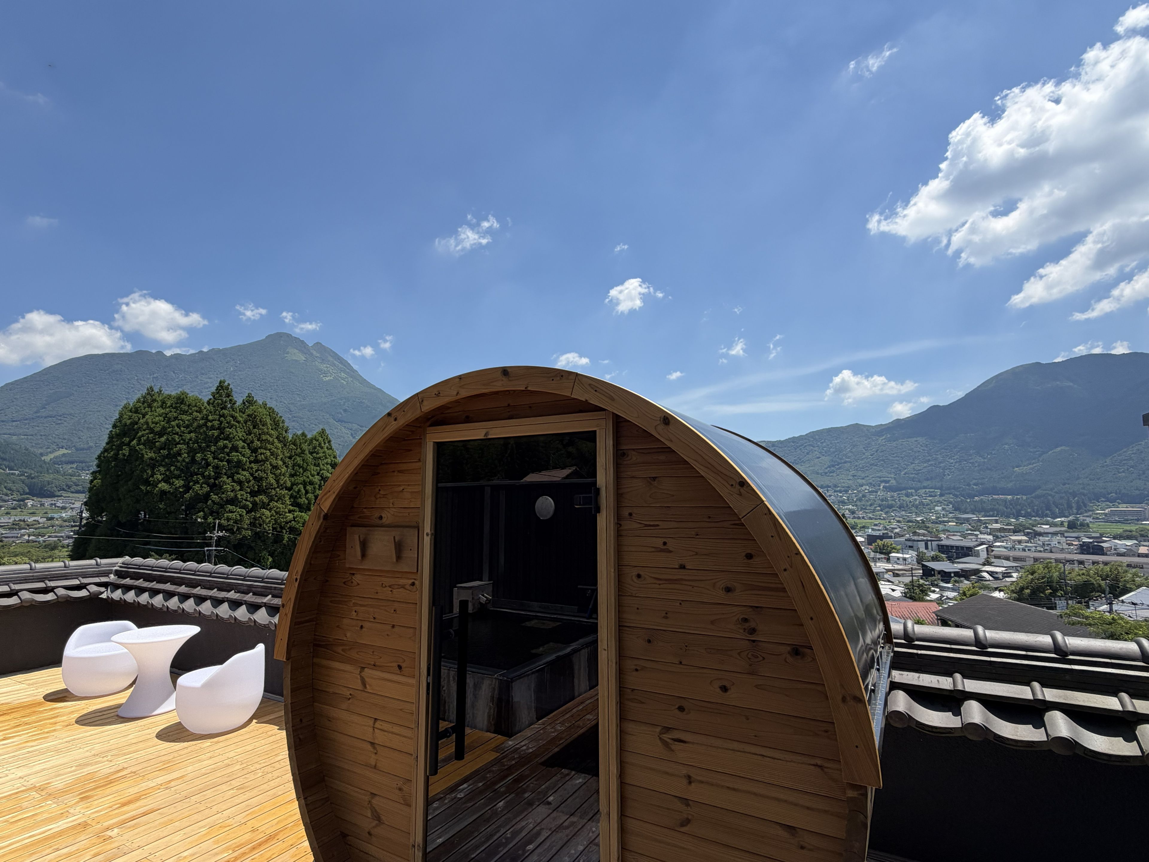 A wooden cabin with a curved roof, a small bathroom, and a deck with white chairs.