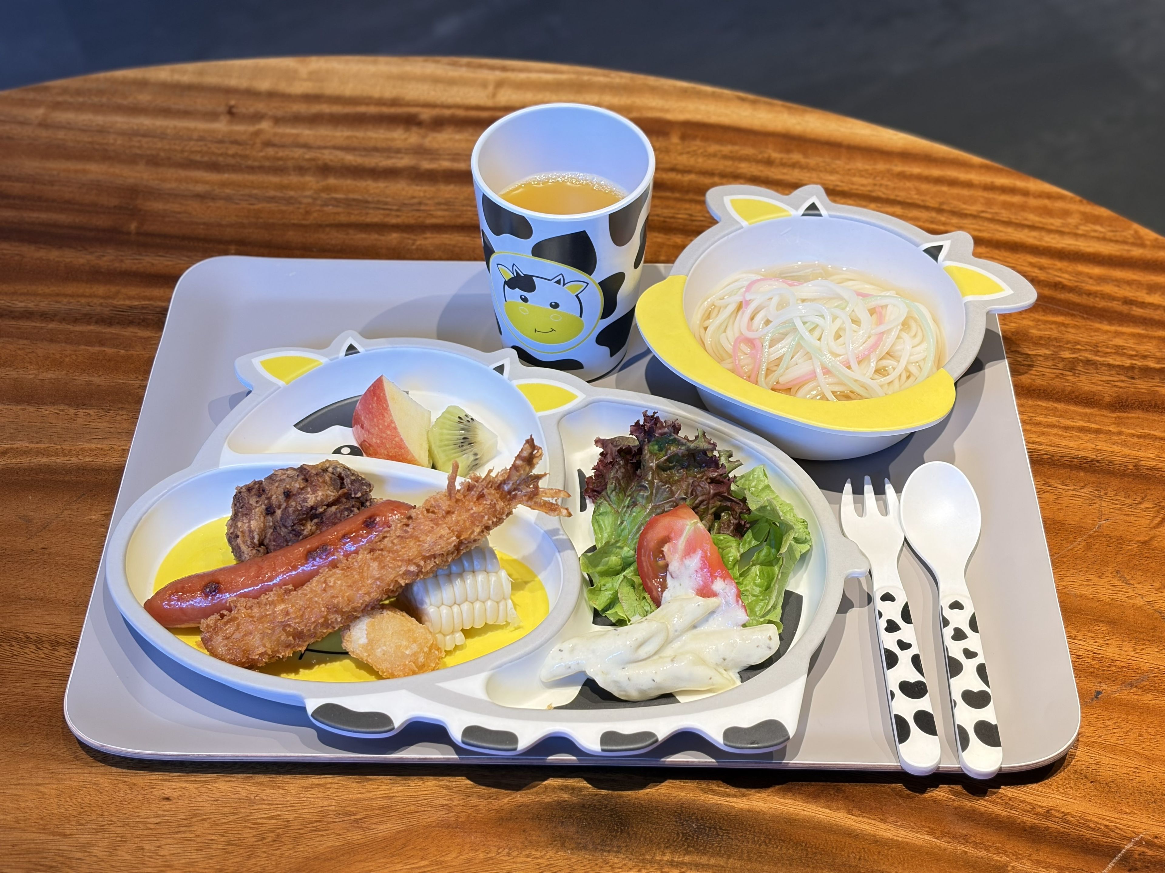 A tray with a meal consisting of a salad, a piece of meat, a fried item, and a bowl of noodles.