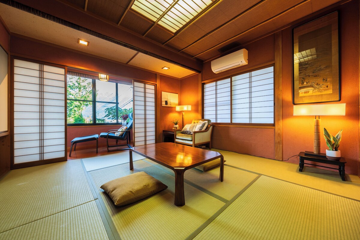 Une pièce de style japonais traditionnel, avec un sol recouvert de tatamis, une table basse, un canapé et des portes coulissantes.