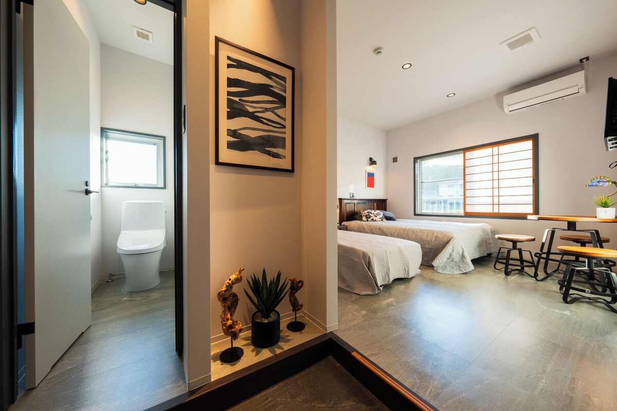 A modern hotel room with a large bed, a small desk, and a window with blinds.