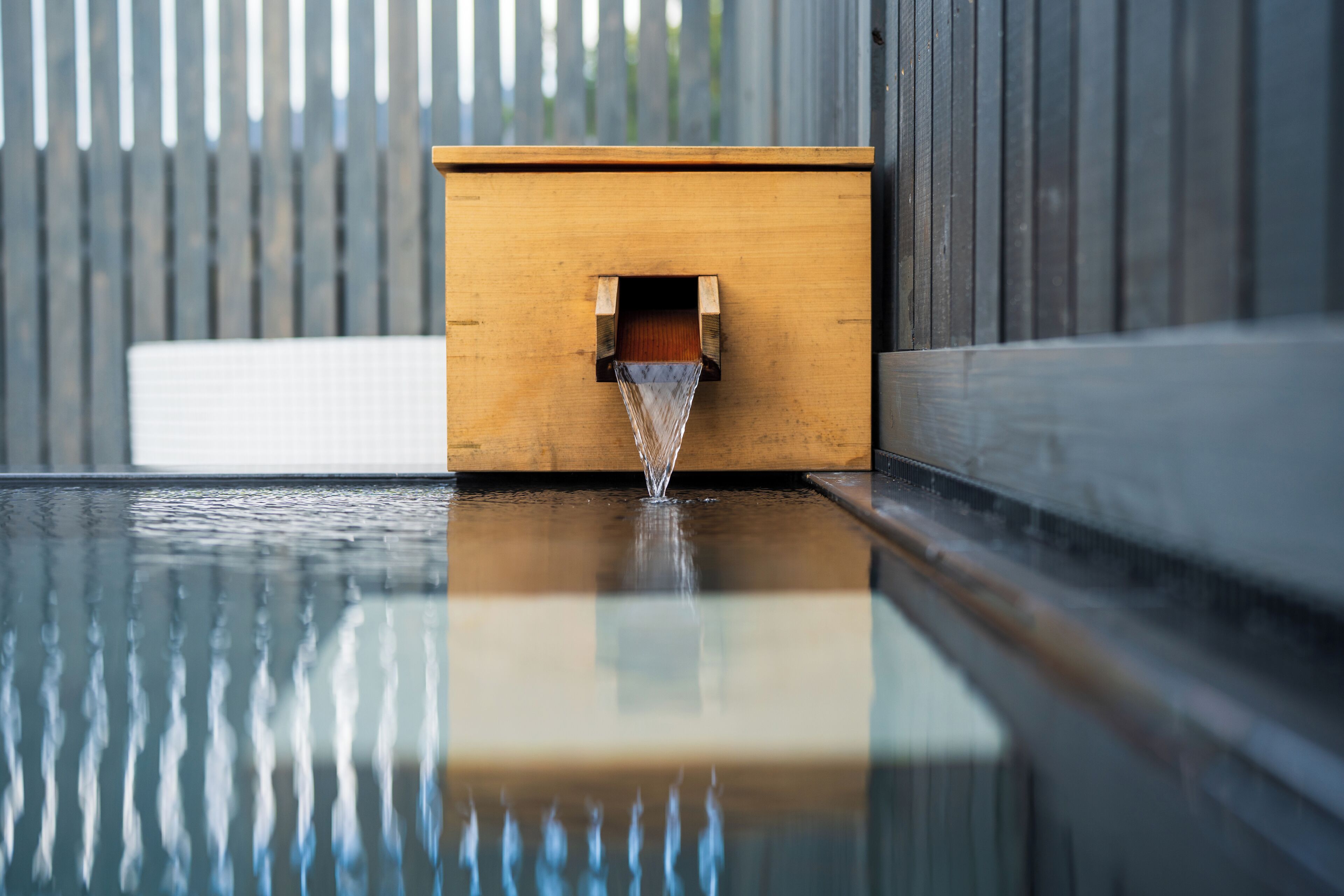 A wooden water feature with a clear water spout, reflecting on a glass surface.