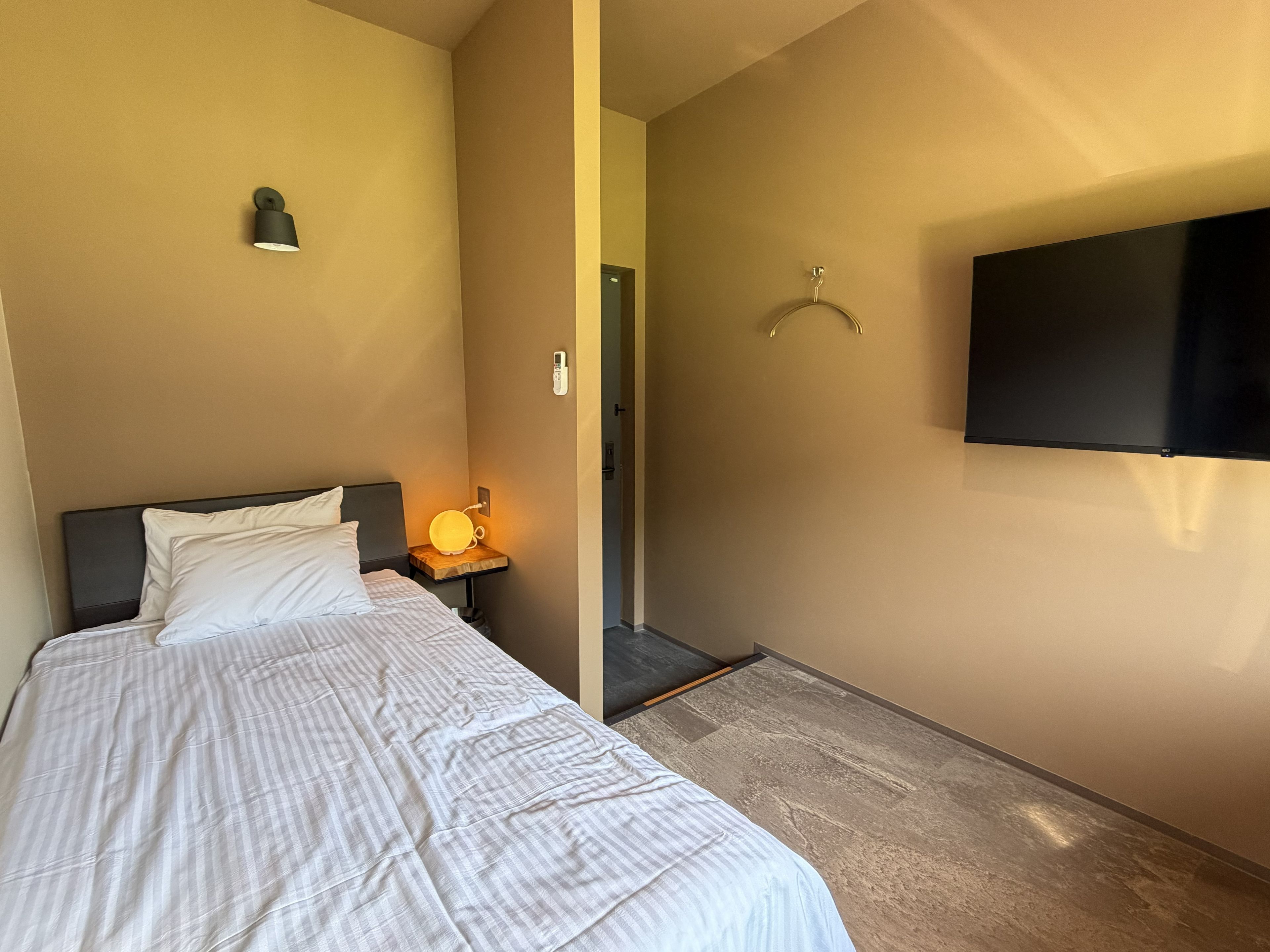 A hotel room with a bed, bedside lamp, and a mounted television.
