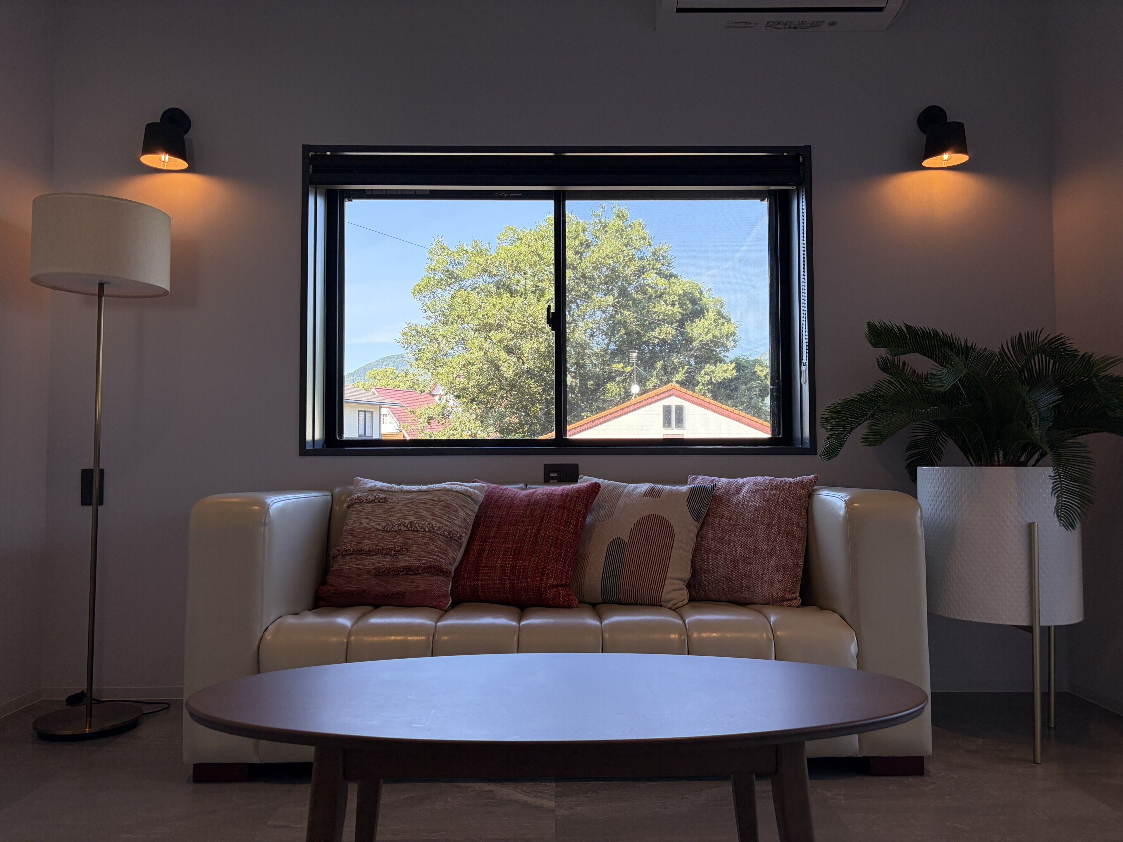 Un salón moderno con un sofá color beige, una mesa de centro redonda y dos lámparas fijadas a la pared.