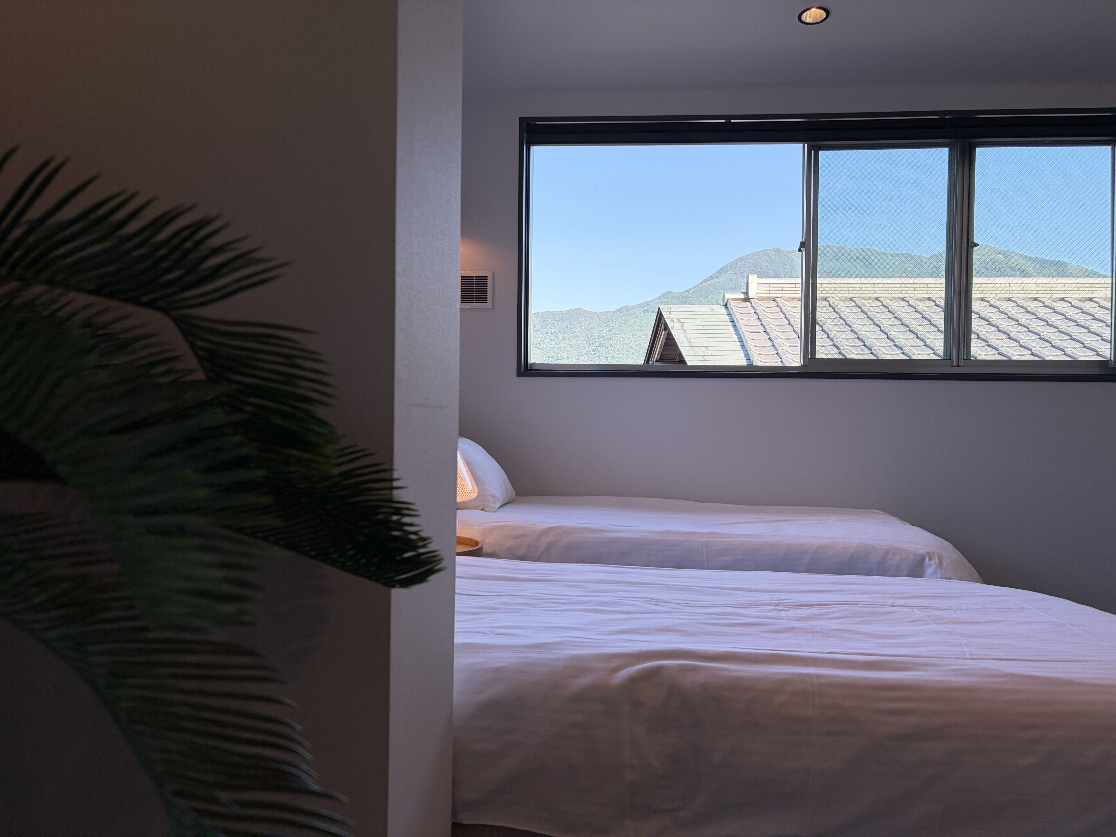 A room with two beds, a large window with a view of mountains, and a potted plant.