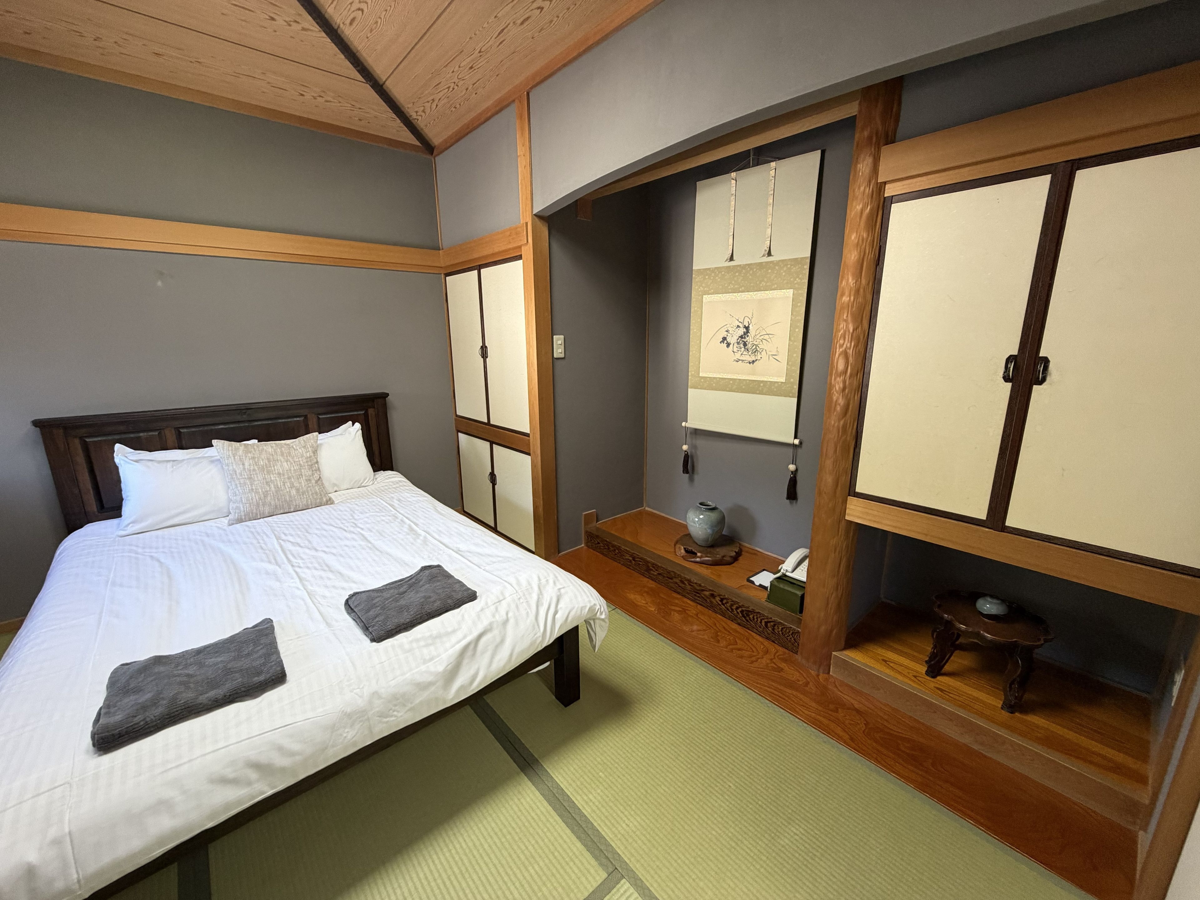 Une pièce de style japonais traditionnel, avec un sol recouvert de tatamis, un lit avec une literie blanche, une tête de lit en bois et des portes coulissantes.