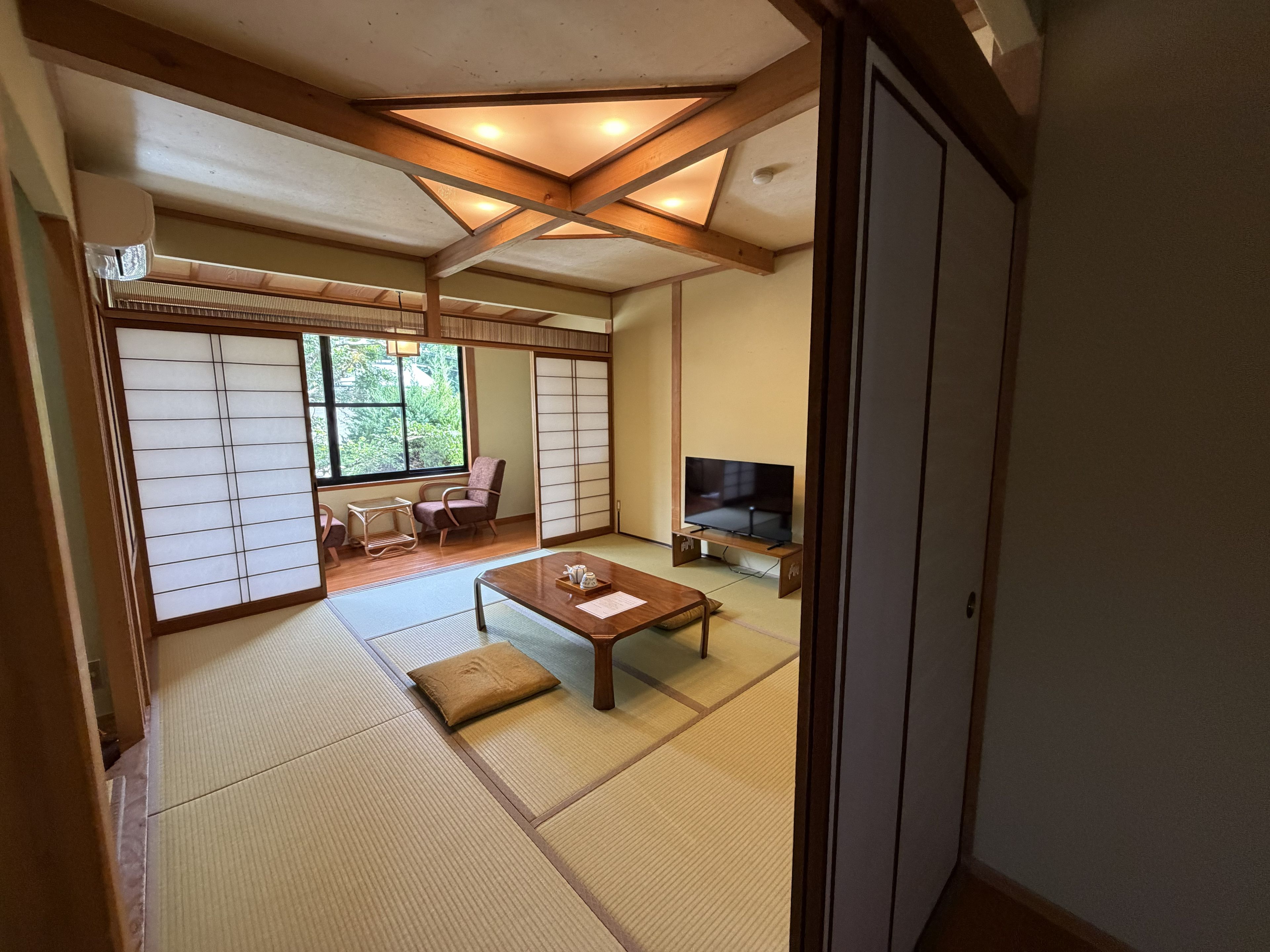 A traditional Japanese room with tatami flooring, a low wooden table, a television, and sliding doors.