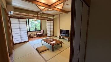 A traditional Japanese room with tatami flooring, a low wooden table, a television, and sliding doors.