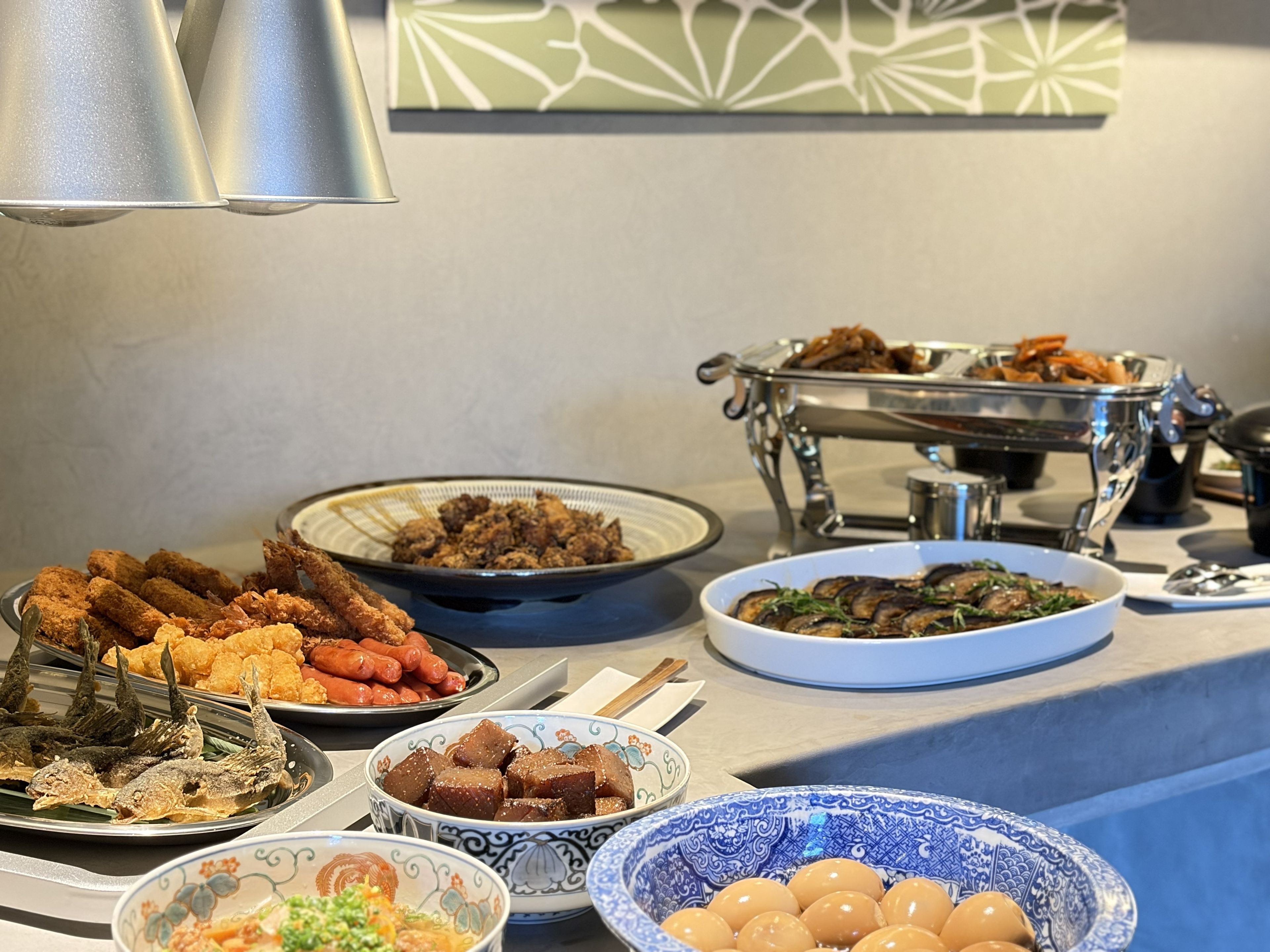 A buffet table with various dishes including fried fish, sausages, and a bowl of eggs.