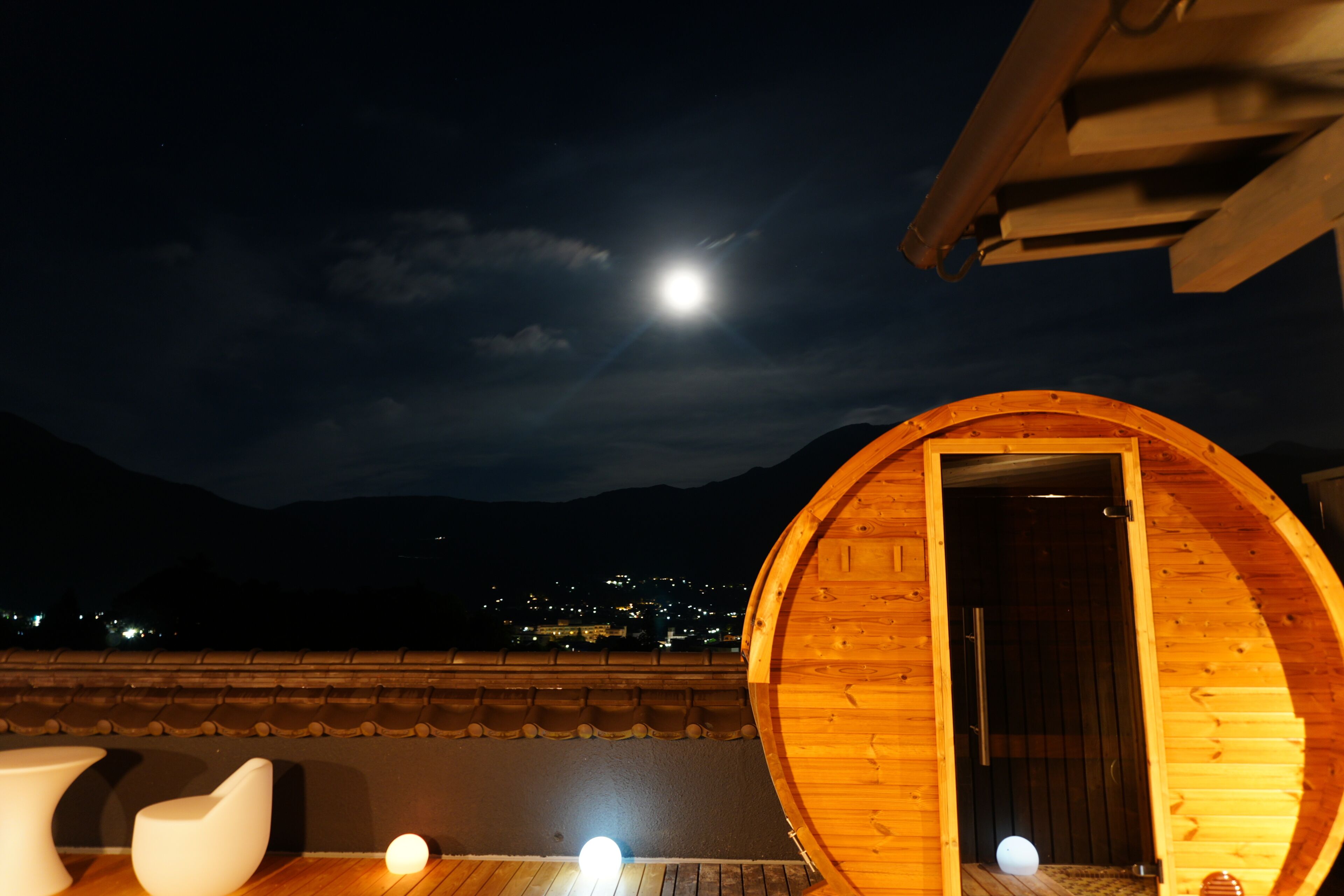 A wooden structure with a circular door, a small light source on the ground, and a view of a mountain range in the background.
