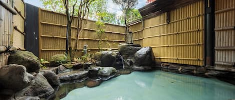 A traditional Japanese onsen with a clear pool, bamboo walls, and large rocks.