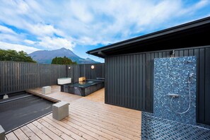 Un moderno espacio exterior con spa, que incluye un deck de madera, un jacuzzi y un recinto de ducha con mosaicos.