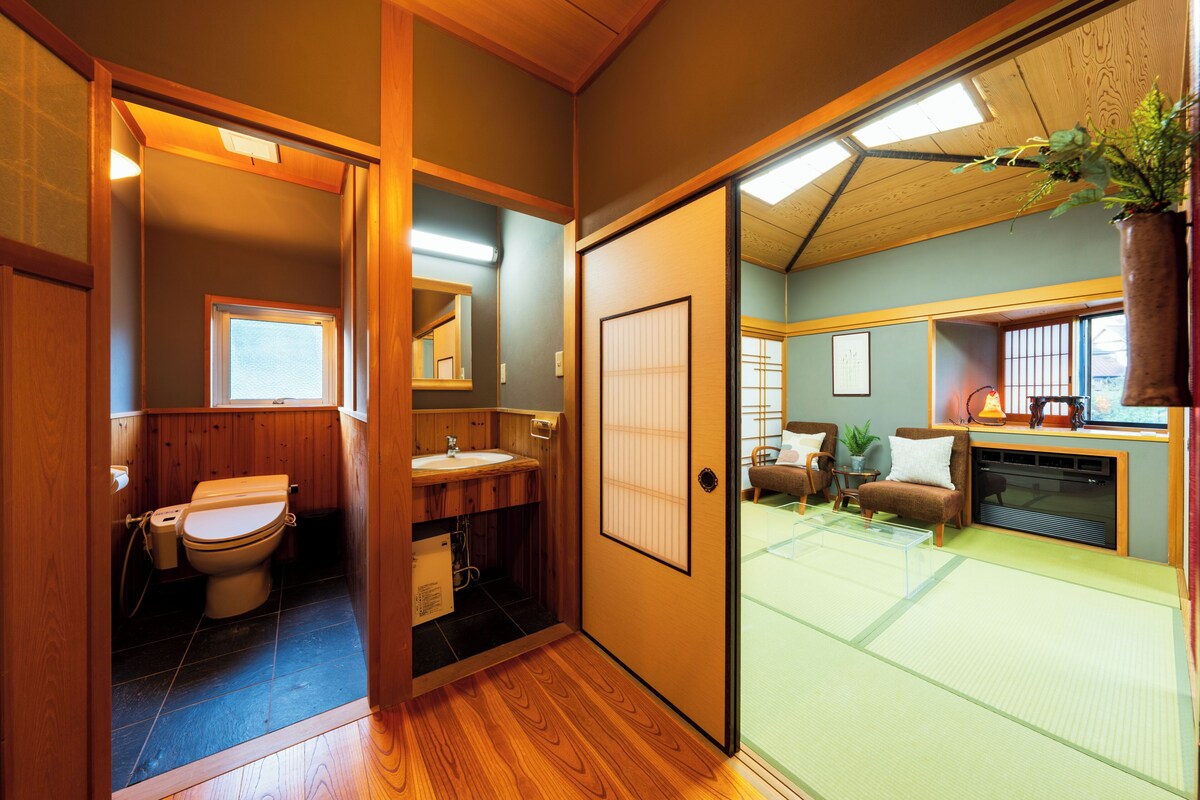 A traditional Japanese-style room with a wooden floor, a tatami mat area, a toilet, a sink, and a sliding door leading to a balcony.
