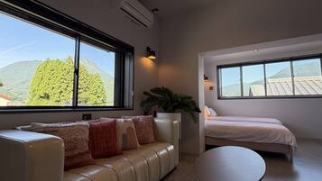 A modern room with a sofa, a round table, and a bed, featuring large windows with a mountain view.