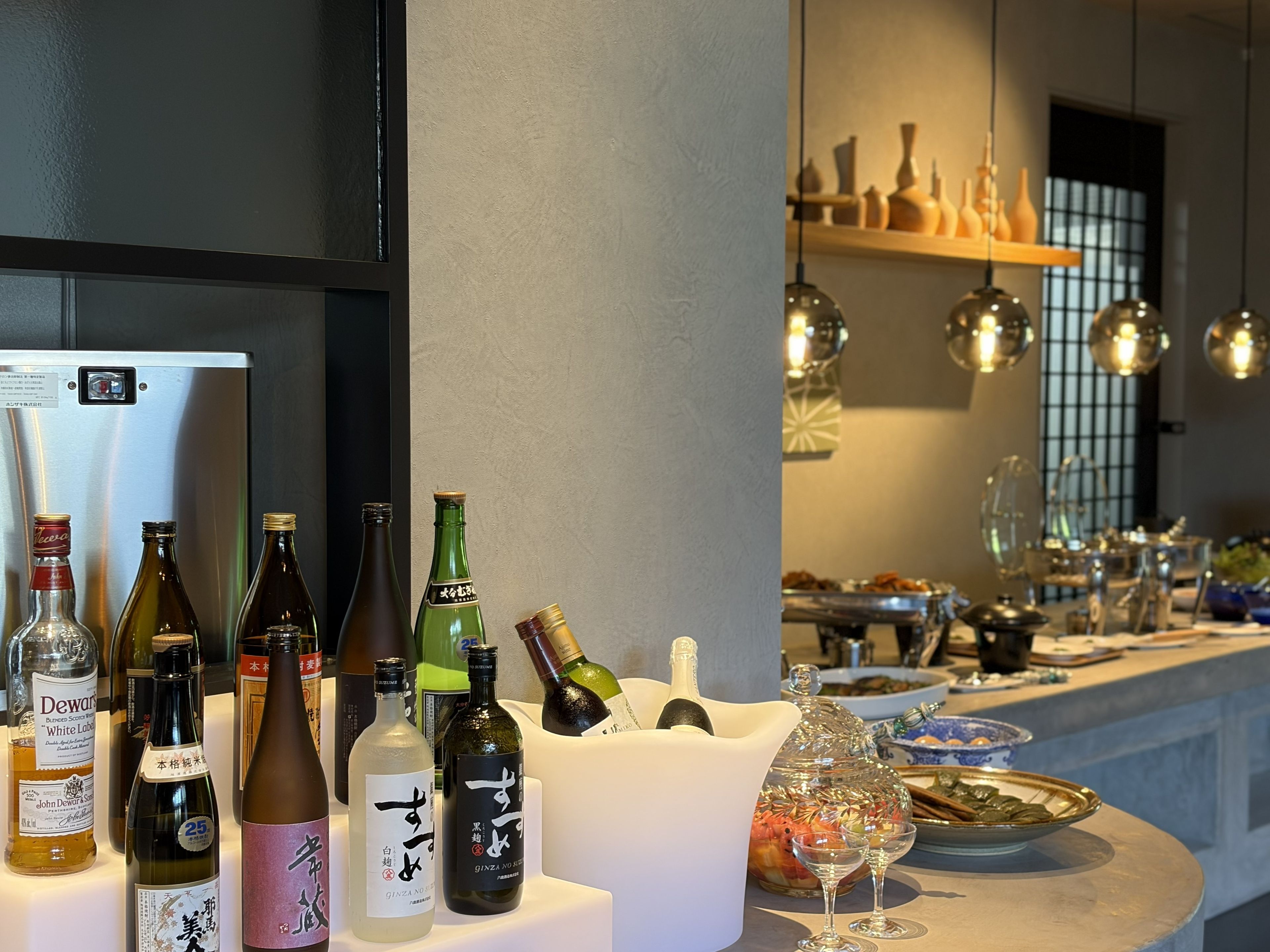 A bar area with various bottles and glasses, a refrigerator, and a shelf with decorative items.