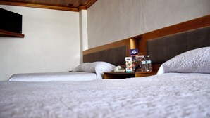 A hotel room with two beds, a wooden headboard, a nightstand with a phone and magazines, and a wall-mounted TV. - Hotel Rio Inn (Aguascalientes)