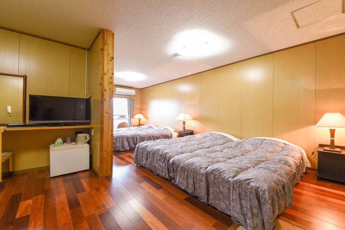 Una habitación con dos camas, televisión, una mesita con lámpara y ventana.
