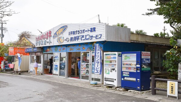 Fachada con un letrero azul y blanco, una máquina expendedora y una pequeña entrada a una tienda.