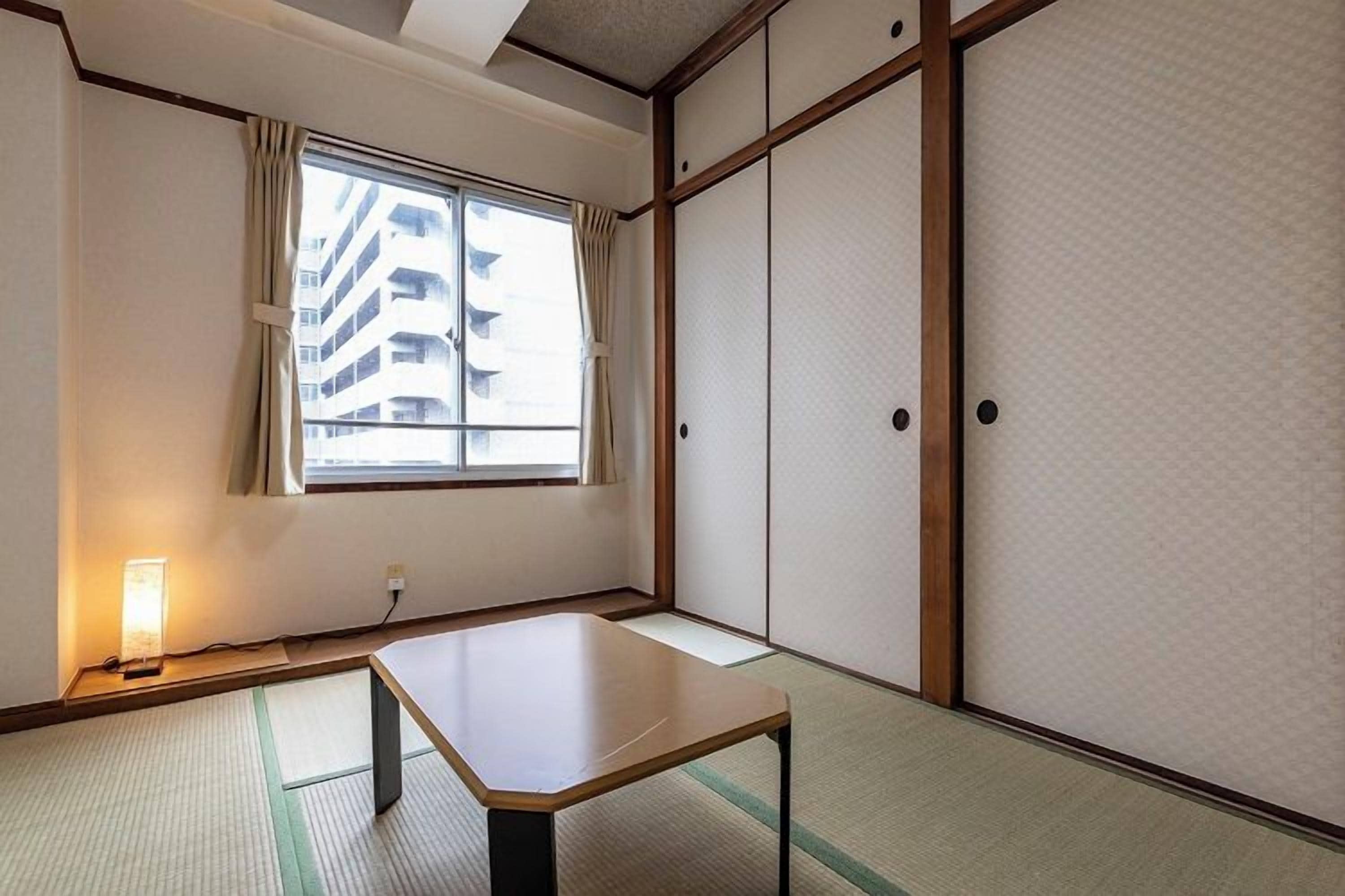 A traditional Japanese room with tatami flooring, a low table, sliding doors, and a window with curtains.