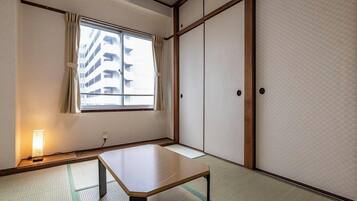 A traditional Japanese room with tatami flooring, a low table, sliding doors, and a window with curtains.